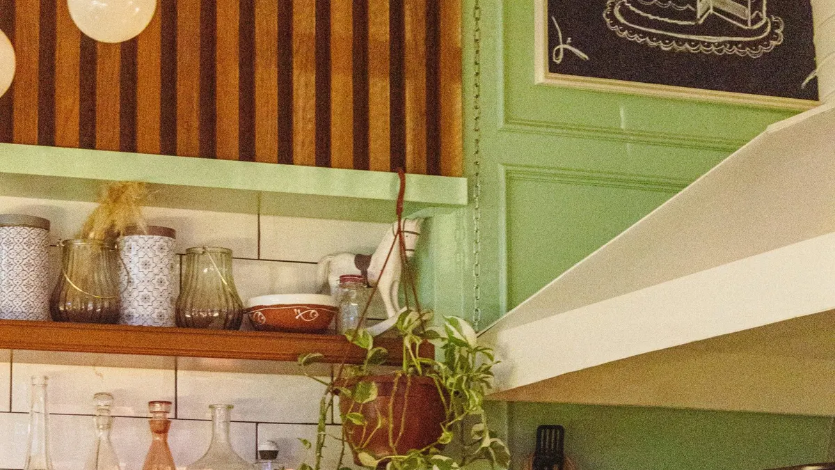 Interior de café de bairro com prateleiras de madeira, louças e plantas penduradas